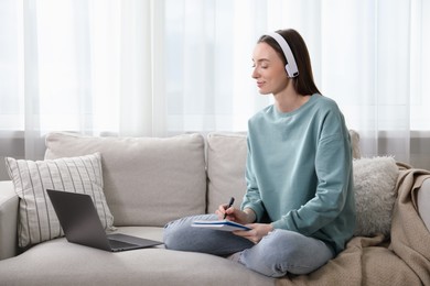 Photo of Woman taking notes during online lesson on sofa indoors. Self-study