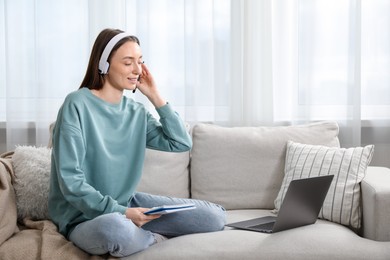 Photo of Smiling woman learning online using laptop on sofa indoors. Self-study