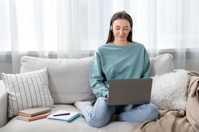 Photo of Woman learning online using laptop on sofa indoors. Self-study