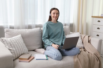 Photo of Smiling woman learning online using laptop on sofa indoors. Self-study