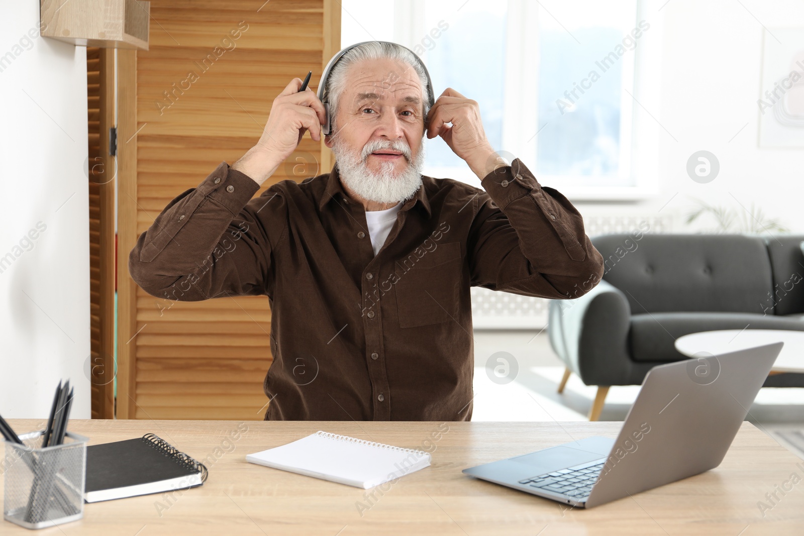 Photo of Senior man learning online using laptop at desk indoors. Self-study