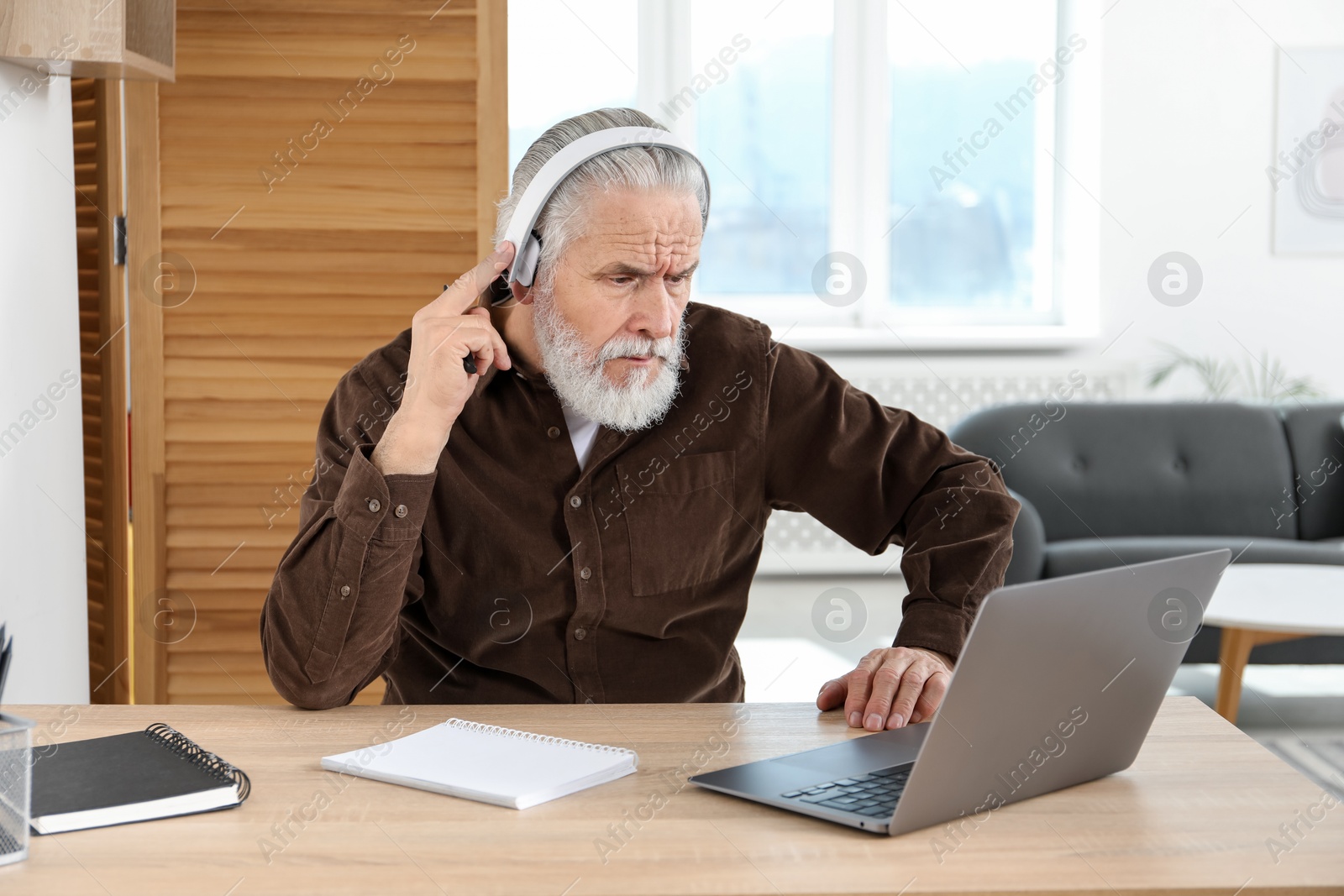 Photo of Senior man learning online using laptop at desk indoors. Self-study