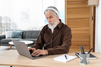 Photo of Senior man learning online using laptop at desk indoors. Self-study