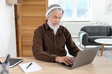 Photo of Senior man learning online using laptop at desk indoors. Self-study