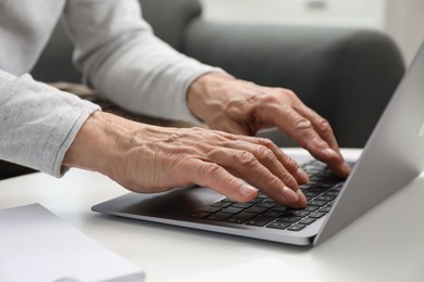 Photo of Senior man using laptop at table indoors, closeup