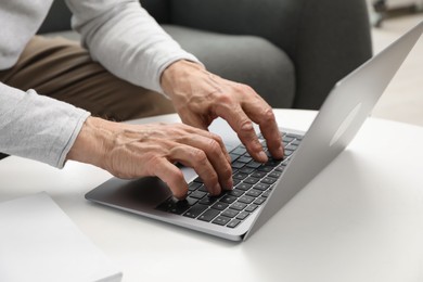 Photo of Senior man using laptop at table indoors, closeup