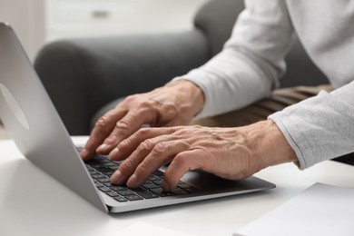 Photo of Senior man using laptop at table indoors, closeup