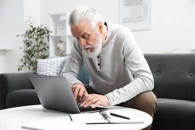 Photo of Senior man learning online using laptop at table indoors. Self-study