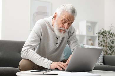 Photo of Senior man learning online using laptop at table indoors. Self-study