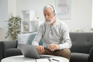 Photo of Senior man learning online using laptop at table indoors. Self-study