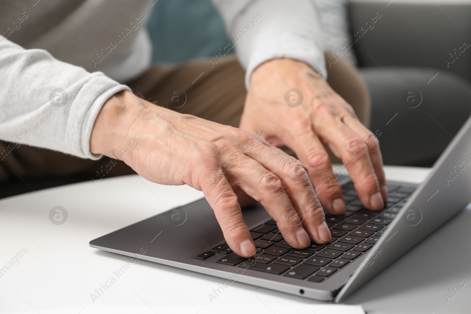 Photo of Senior man using laptop at table indoors, closeup