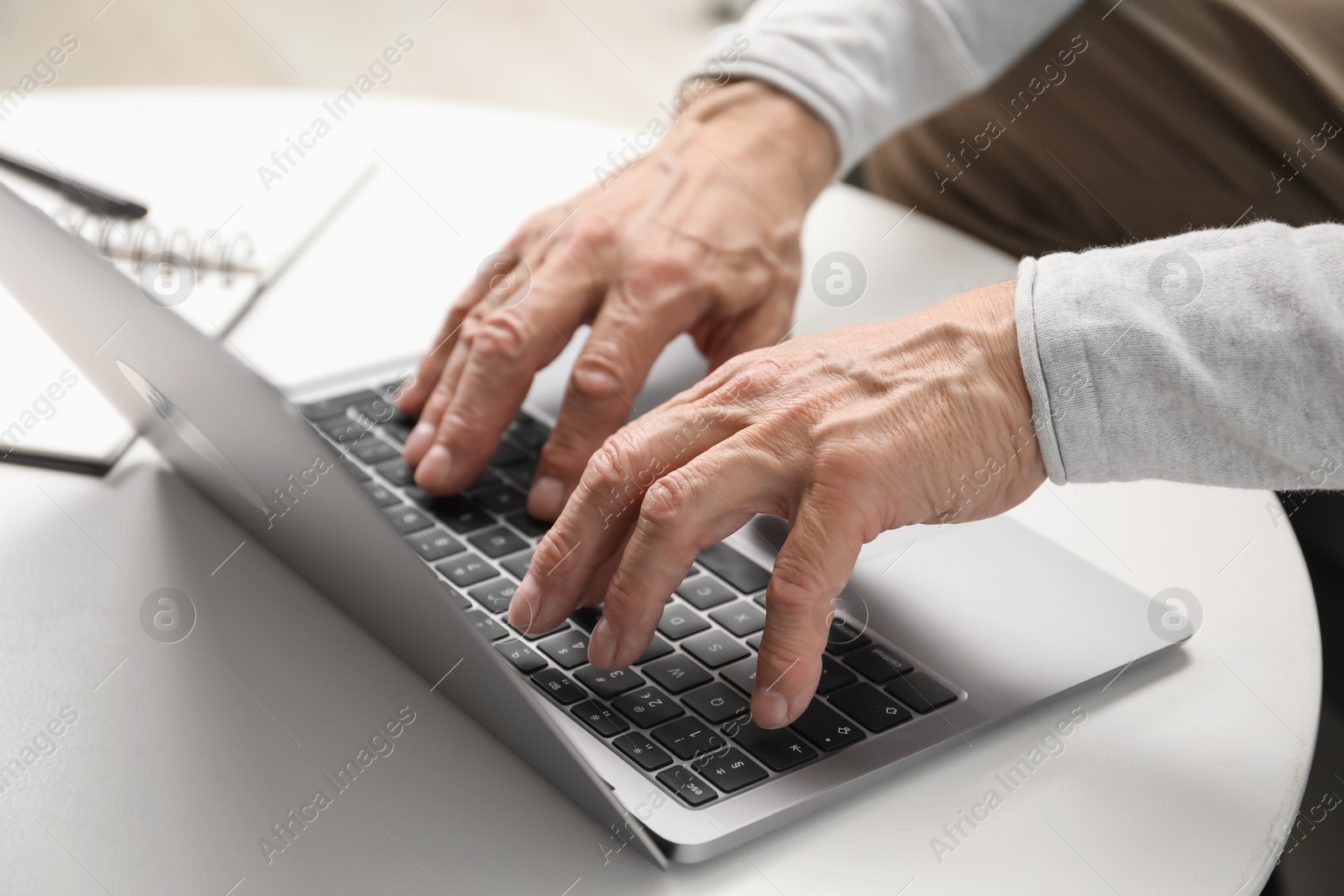 Photo of Senior man using laptop at table indoors, closeup