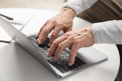 Photo of Senior man using laptop at table indoors, closeup