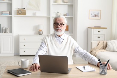 Photo of Senior man learning online using laptop at desk indoors. Self-study