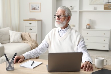 Photo of Senior man learning online using laptop at desk indoors. Self-study