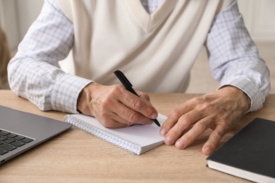 Photo of Senior man taking notes while learning online at desk indoors, closeup. Self-study