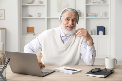 Photo of Senior man learning online using laptop at desk indoors. Self-study