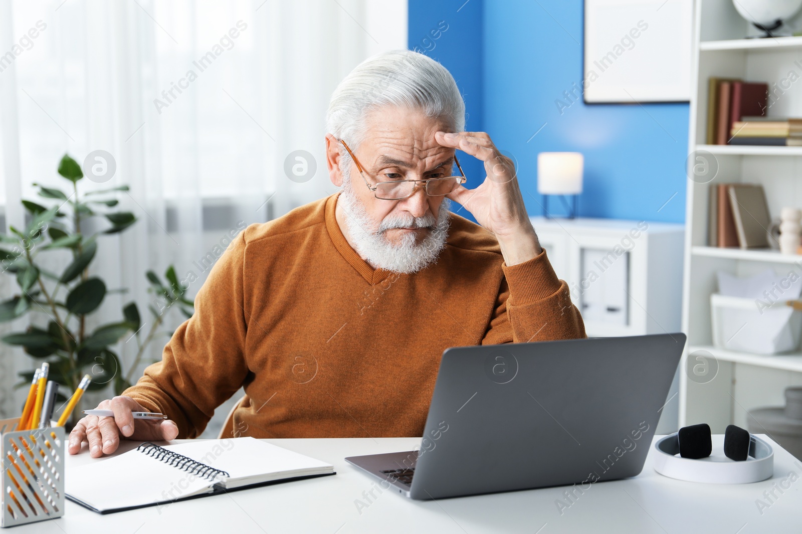 Photo of Senior man learning online using laptop at desk indoors. Self-study