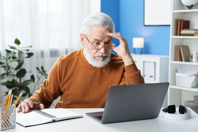 Photo of Senior man learning online using laptop at desk indoors. Self-study