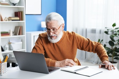 Photo of Senior man learning online using laptop at desk indoors. Self-study