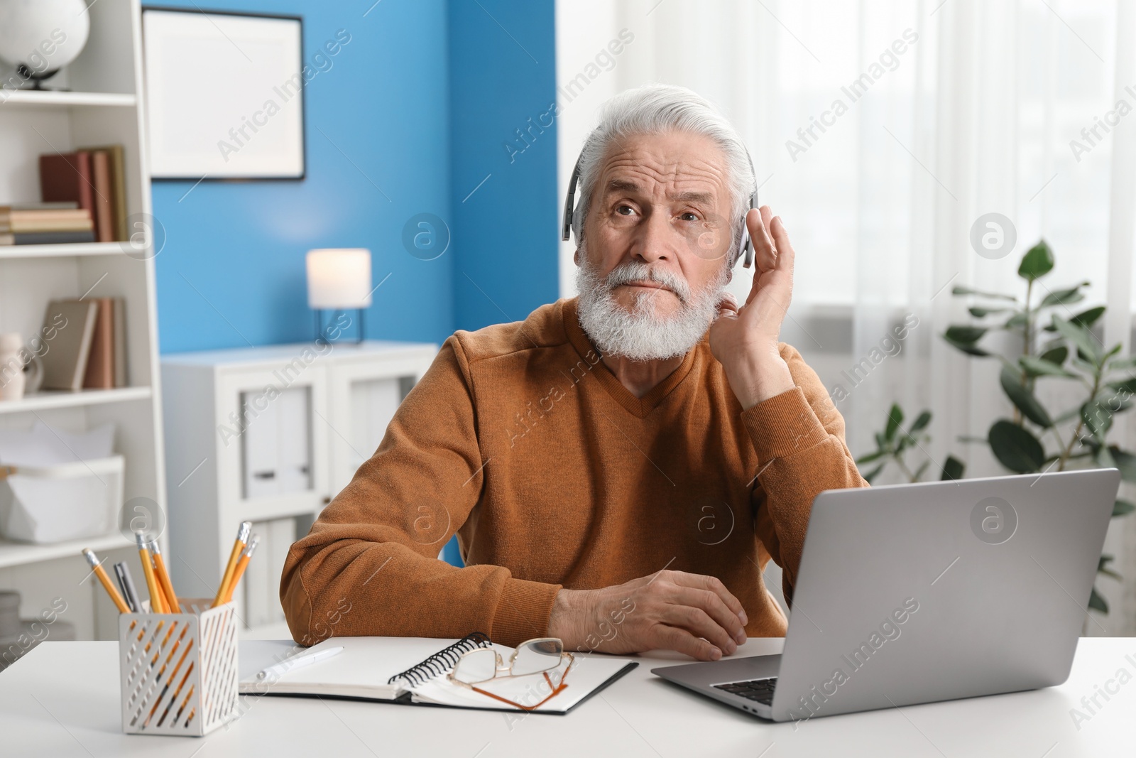 Photo of Senior man learning online using laptop at desk indoors. Self-study