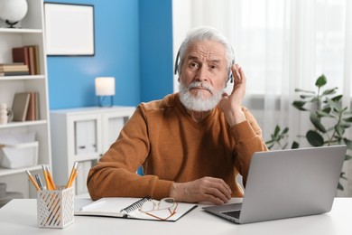 Photo of Senior man learning online using laptop at desk indoors. Self-study