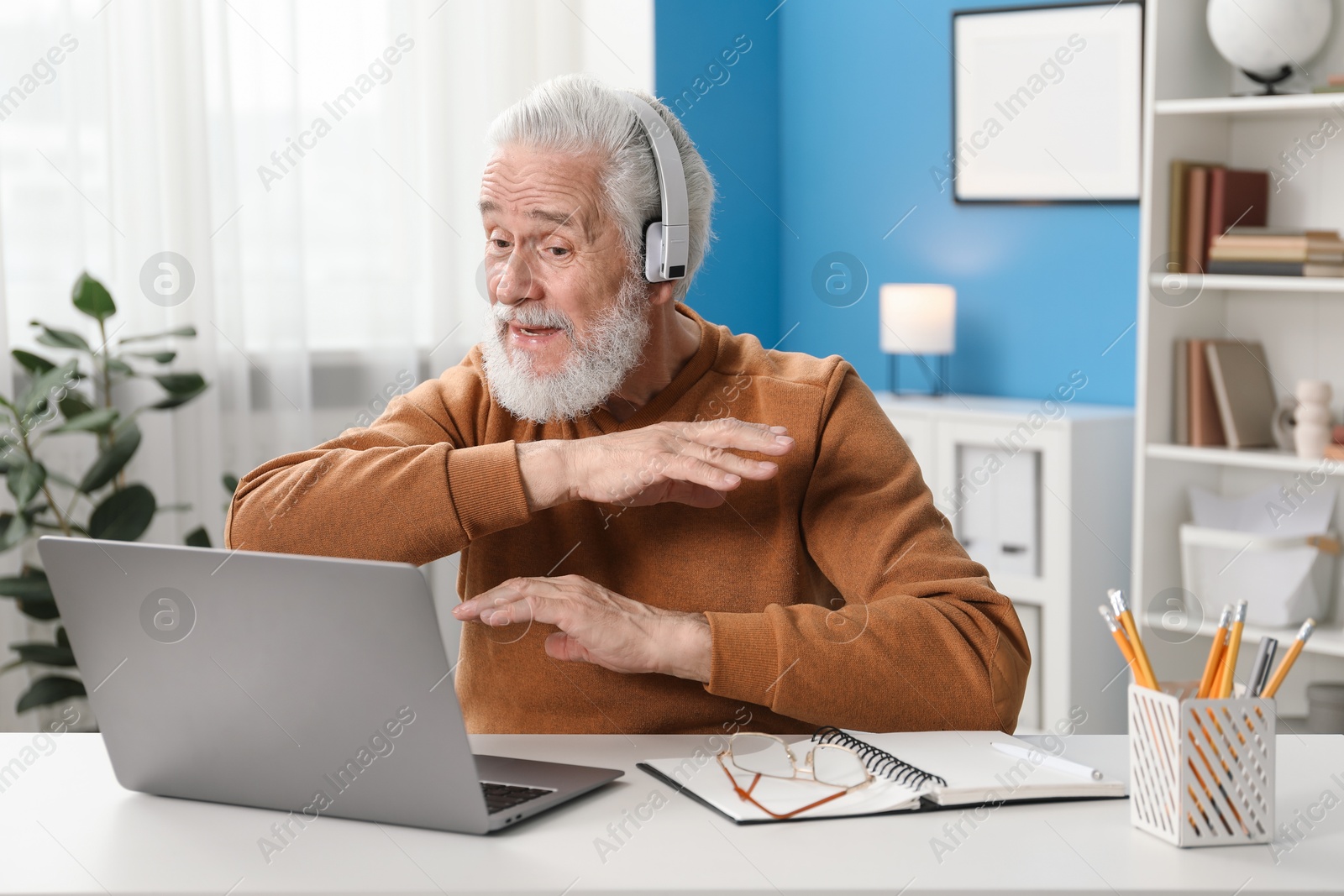 Photo of Senior man having online lesson with teacher at desk indoors. Self-study