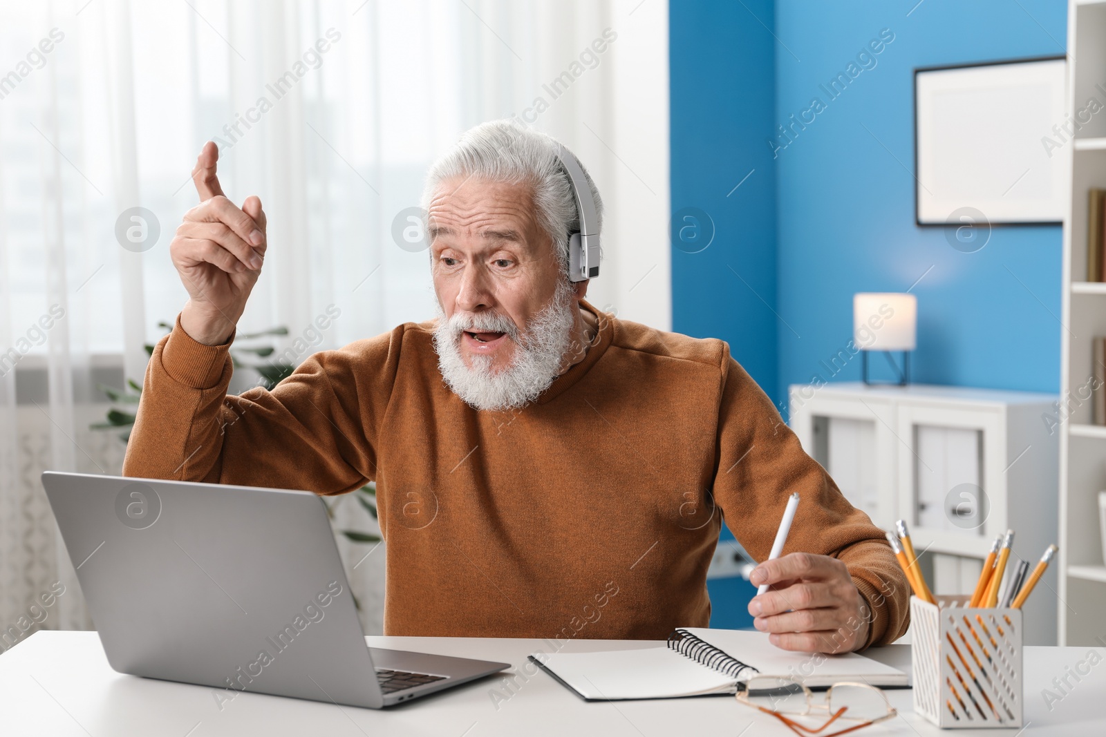 Photo of Senior man having online lesson with teacher at desk indoors. Self-study