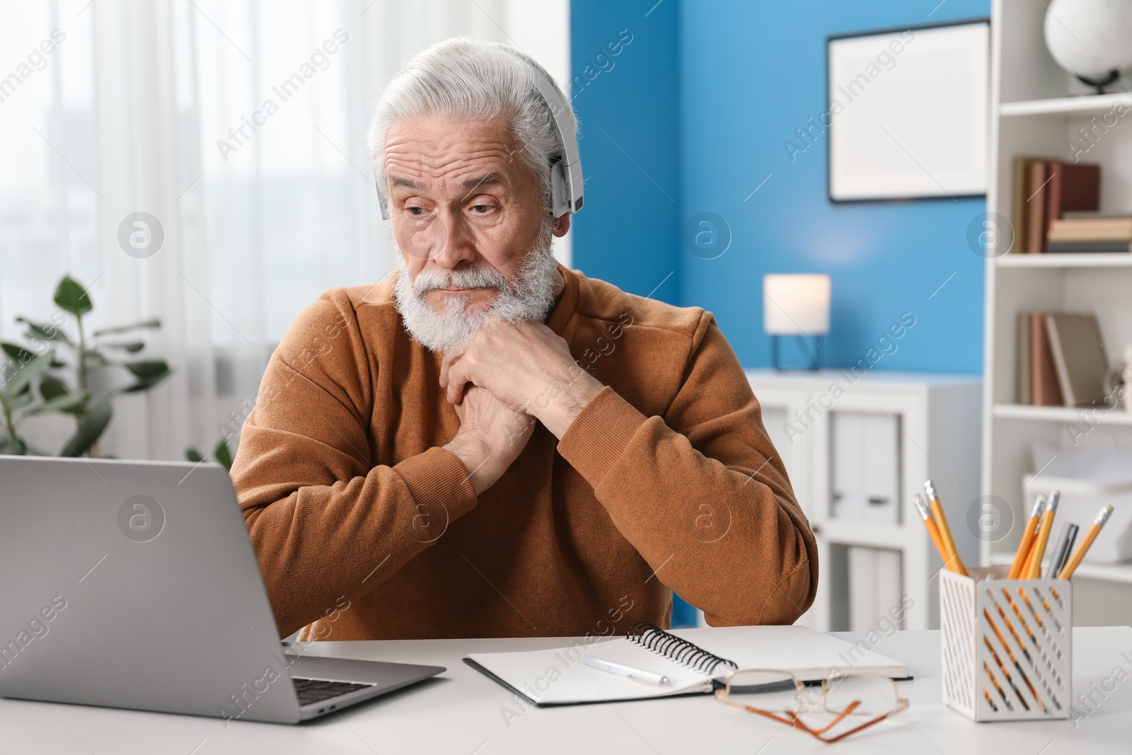 Photo of Senior man learning online using laptop at desk indoors. Self-study