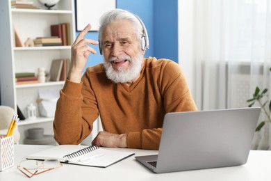 Photo of Senior man learning online using laptop at desk indoors. Self-study