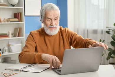 Photo of Senior man learning online using laptop at desk indoors. Self-study