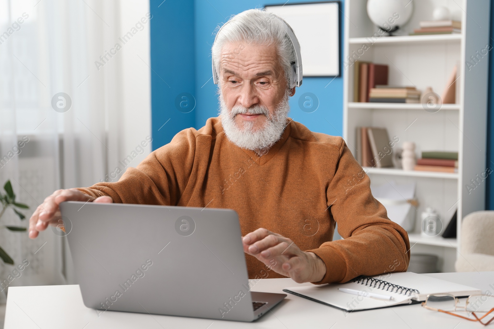 Photo of Senior man learning online using laptop at desk indoors. Self-study