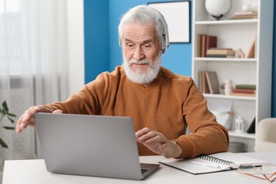 Photo of Senior man learning online using laptop at desk indoors. Self-study