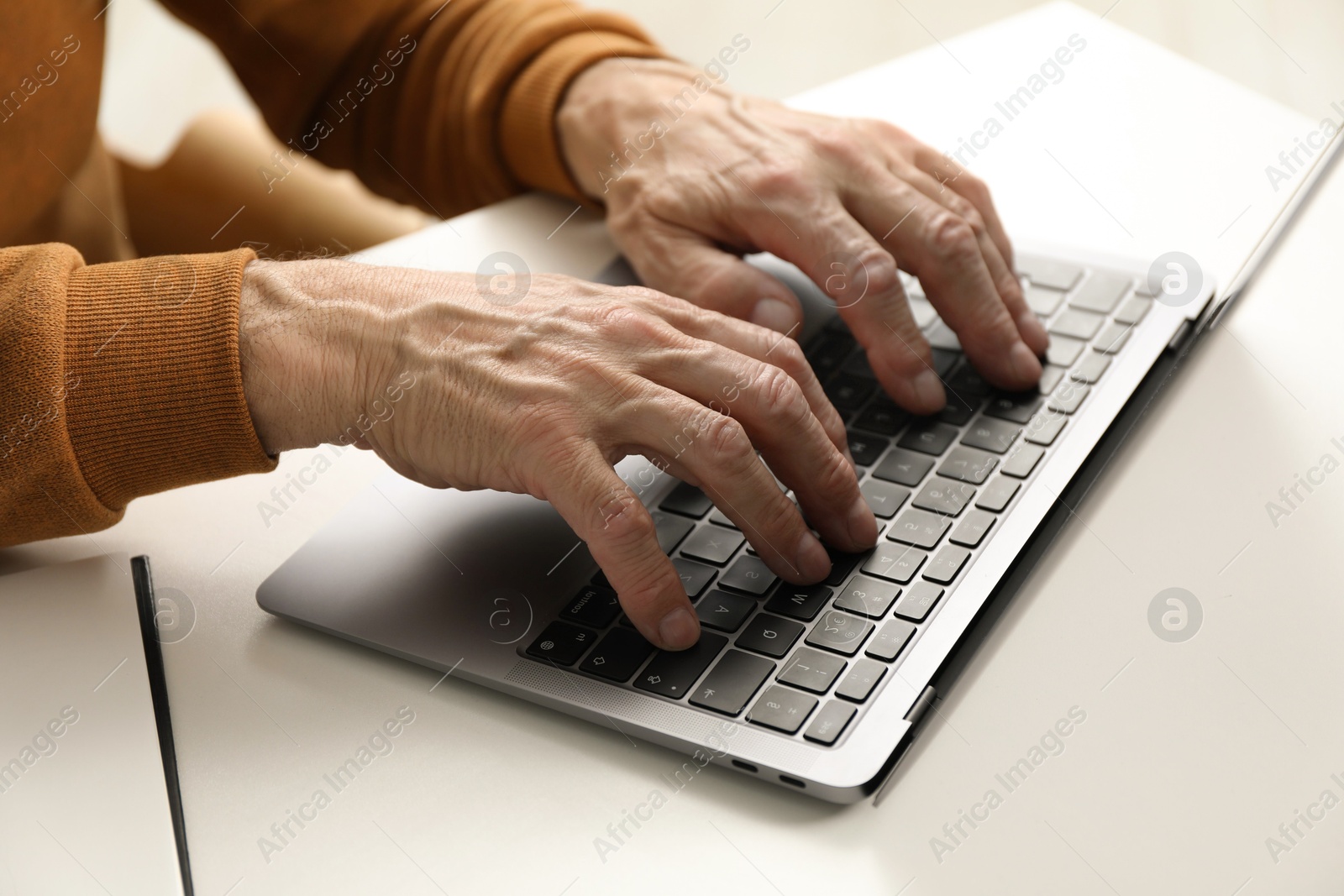 Photo of Senior man using laptop at table indoors, closeup