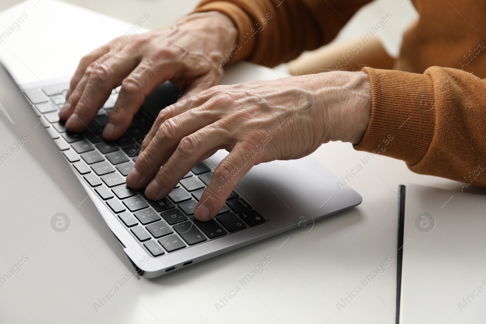 Photo of Senior man using laptop at table indoors, closeup