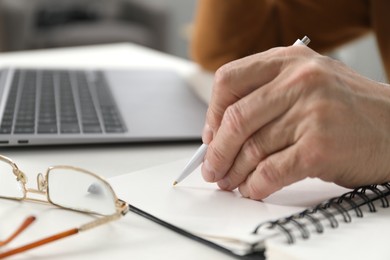 Photo of Senior man taking notes while learning online at desk indoors, closeup. Self-study