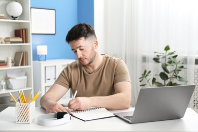 Photo of Man taking notes during online lesson at desk indoors. Self-study