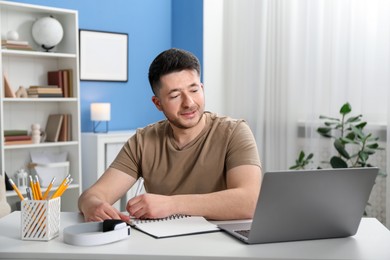 Photo of Man taking notes during online lesson at desk indoors. Self-study