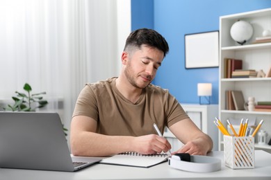 Photo of Man taking notes during online lesson at desk indoors. Self-study