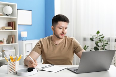 Photo of Man taking notes during online lesson at desk indoors. Self-study