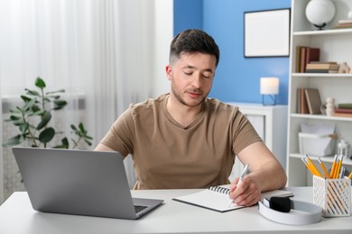 Photo of Man taking notes during online lesson at desk indoors. Self-study