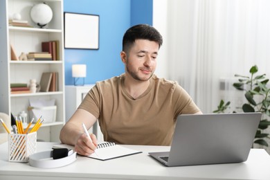 Photo of Man taking notes during online lesson at desk indoors. Self-study