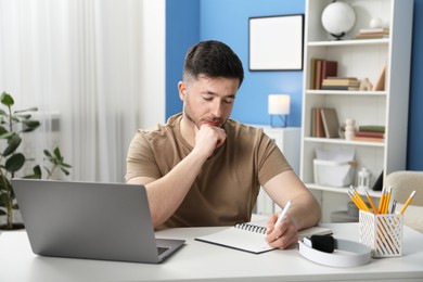 Photo of Man taking notes during online lesson at desk indoors. Self-study