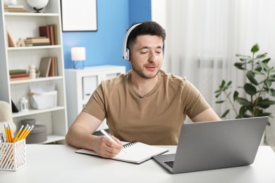 Photo of Man taking notes during online lesson at desk indoors. Self-study