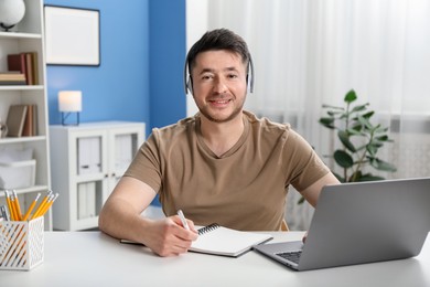 Photo of Man taking notes during online lesson at desk indoors. Self-study