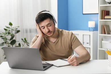 Photo of Man taking notes during online lesson at desk indoors. Self-study