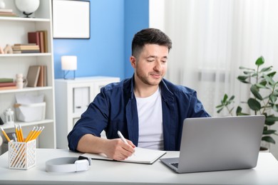 Photo of Man taking notes during online lesson at desk indoors. Self-study