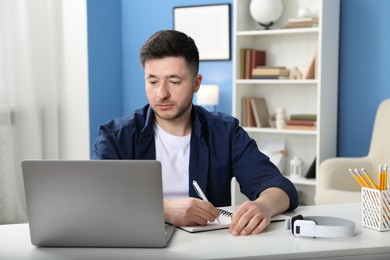 Photo of Man taking notes during online lesson at desk indoors. Self-study