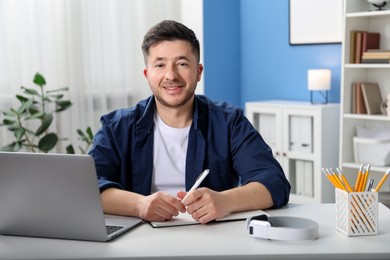 Photo of Man taking notes during online lesson at desk indoors. Self-study