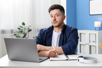 Photo of Man taking notes during online lesson at desk indoors. Self-study